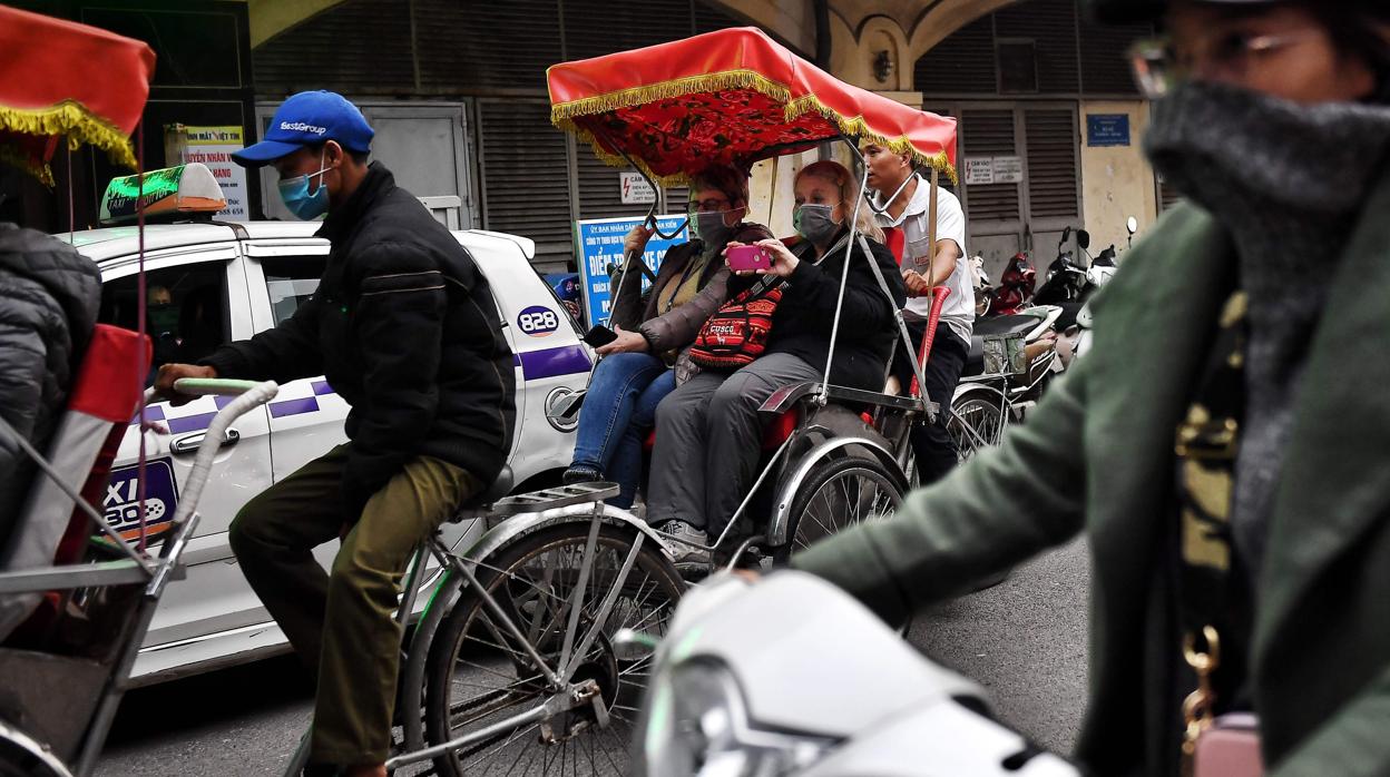 Los turistas con máscaras protectoras montan en un rickshaw por el casco antiguo de Hanoi