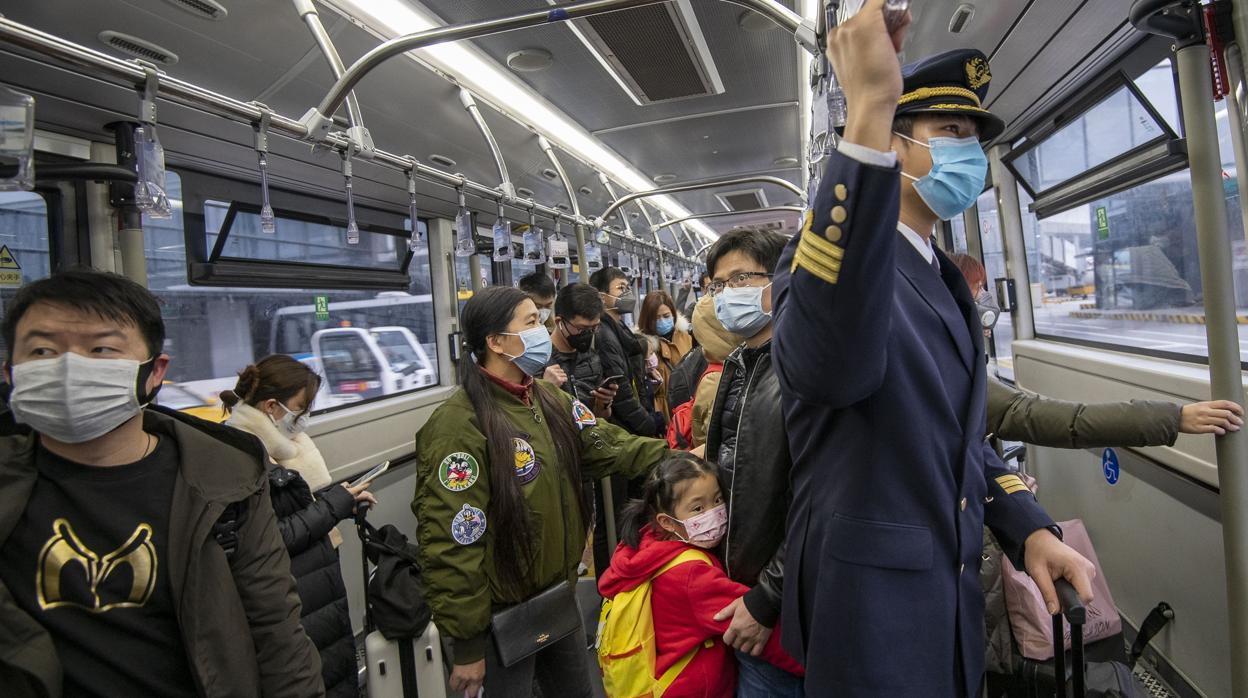 Viajeros y un piloto, todos con máscaras, en un autobús del aeropuerto en Shanghái