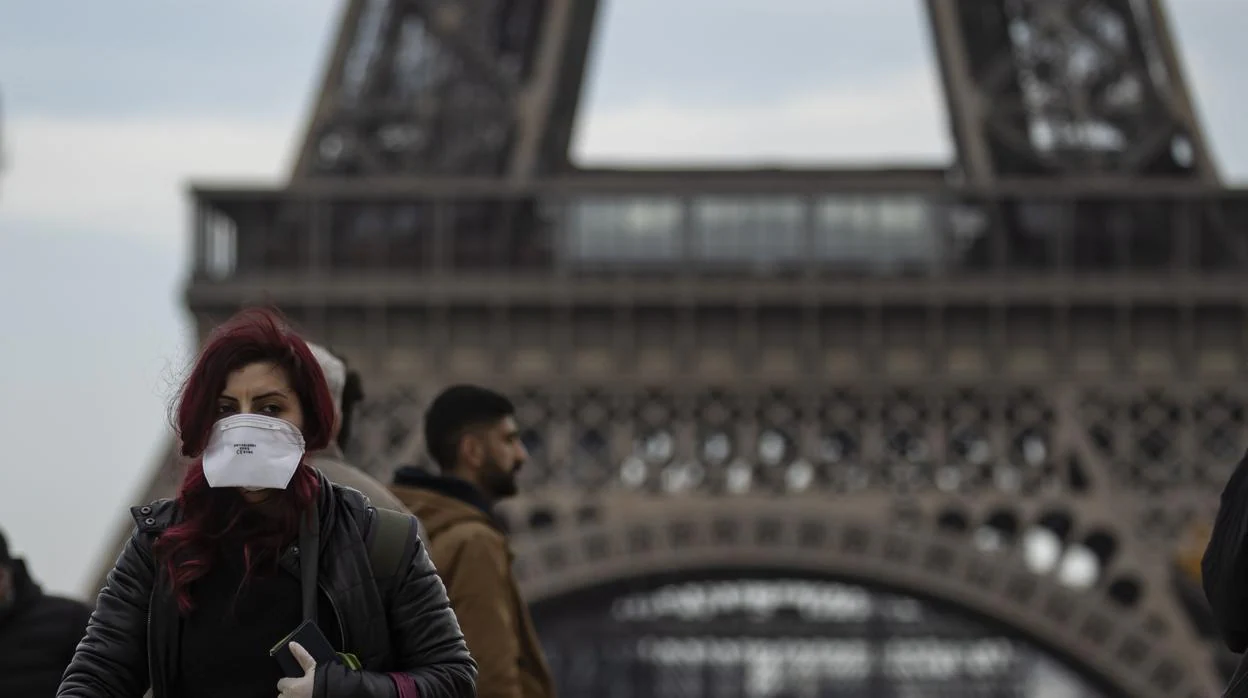 Una mujer pasea frente a la torre Eiffel, símbolo de París, protegida con una mascarilla