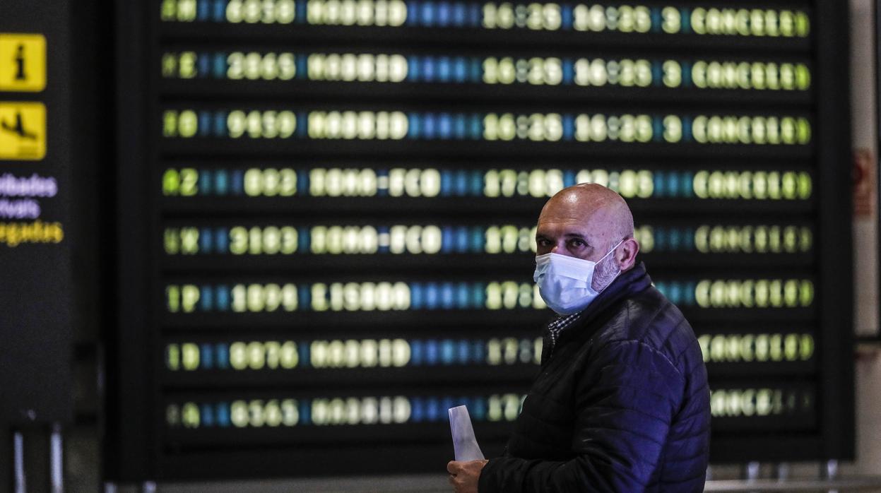 Un hombre con mascarilla mira la pantalla de vuelos durante la crisis por el coronavirus