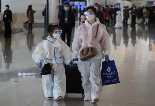 Una madre con su hija, pertrechadas con trajes protectores químicos para tomar un avión en el aeropuerto de Tianhe, en Wuhan