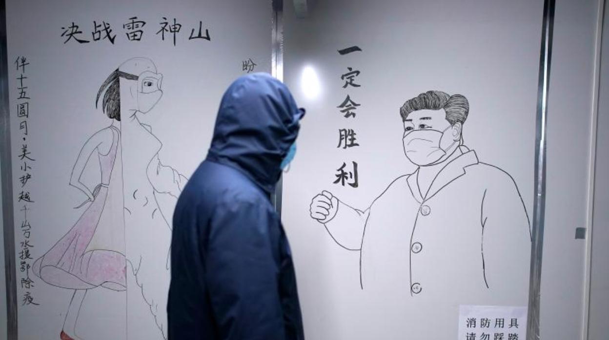 Un miembro del personal pasa por delante de un dibujo del Presidente chino Xi Jinping con una mascarilla situado en una pared del Hospital de Leishenshan (Wuhan)