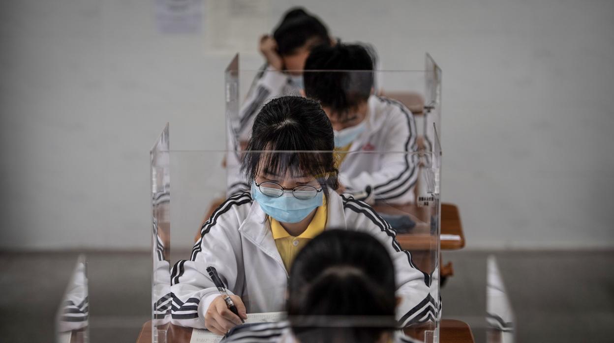 Varios estudiantes, en clase, en fila india, con mamparas y mascarillas