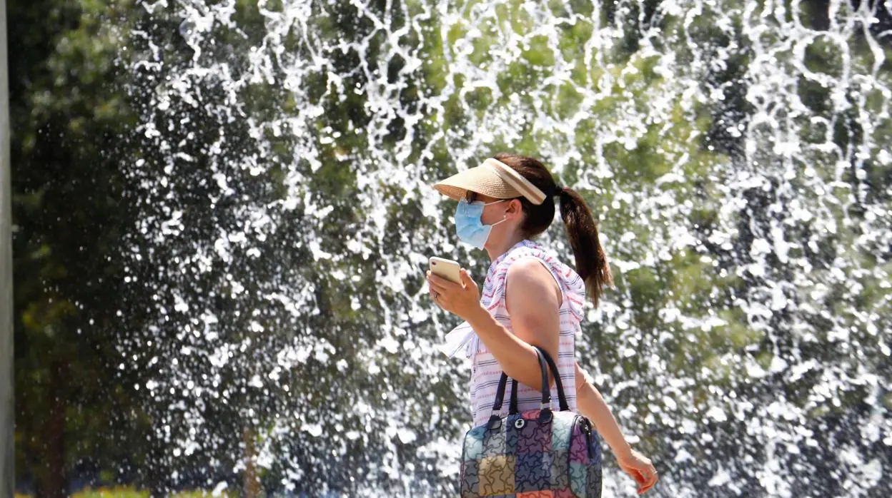 Una mujer protegida con mascarilla y visera pasa junto a una de las fuentes de Córdoba