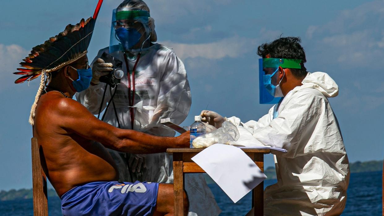 Dos enfermeros le hacen la prueba de coronavirus al líder de un grupo indígena de Brasil