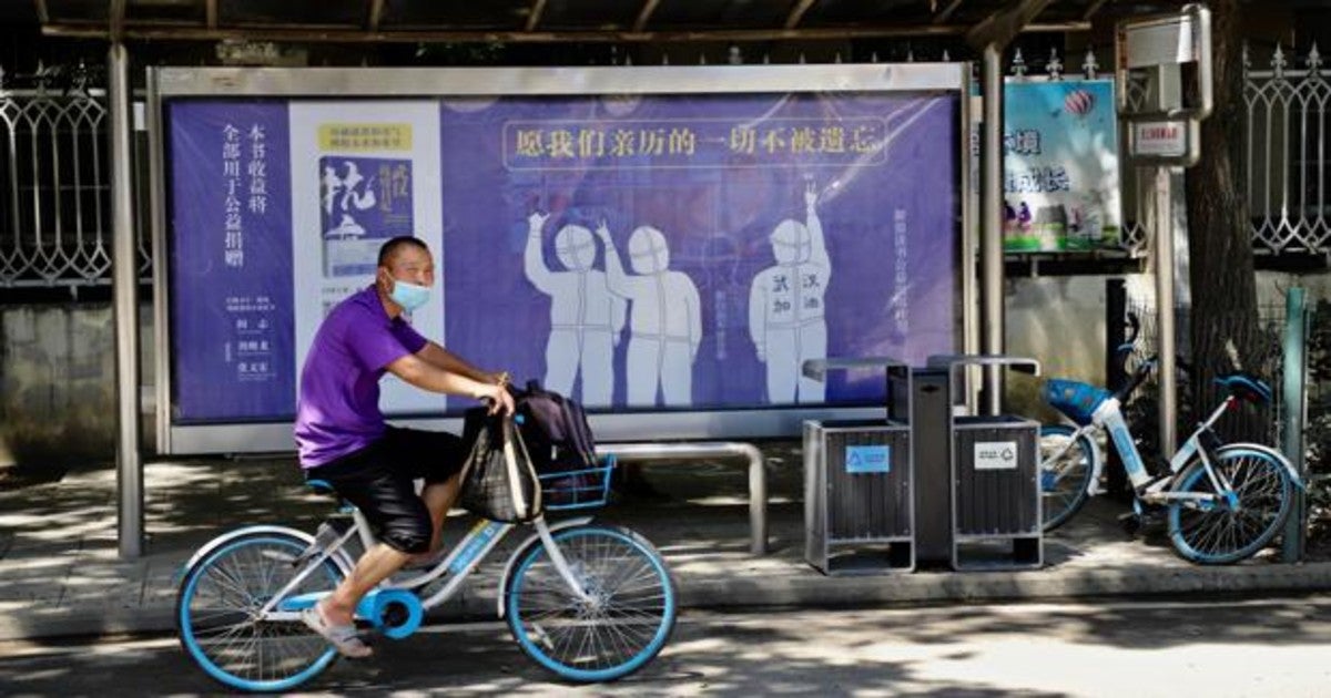 Un ciclista pasa ante una parada de autobús de Wuhan con un anuncio de un libro sobre la lucha contra la pandemia