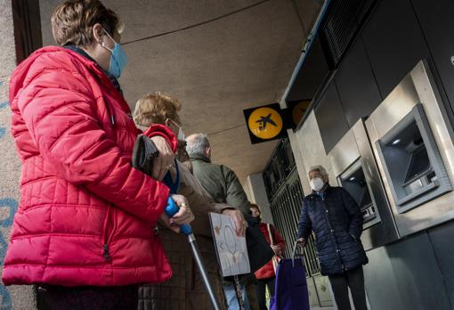 Varias personas jubiladas hacen cola en un cajero en la Comunidad de Madrid