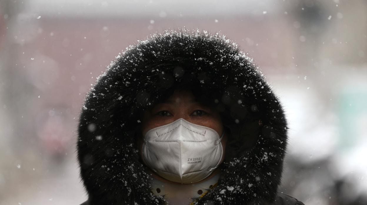 Una mujer con mascarilla camina por una calle mientras nieva en Pekín, China, el 18 de marzo de 2022