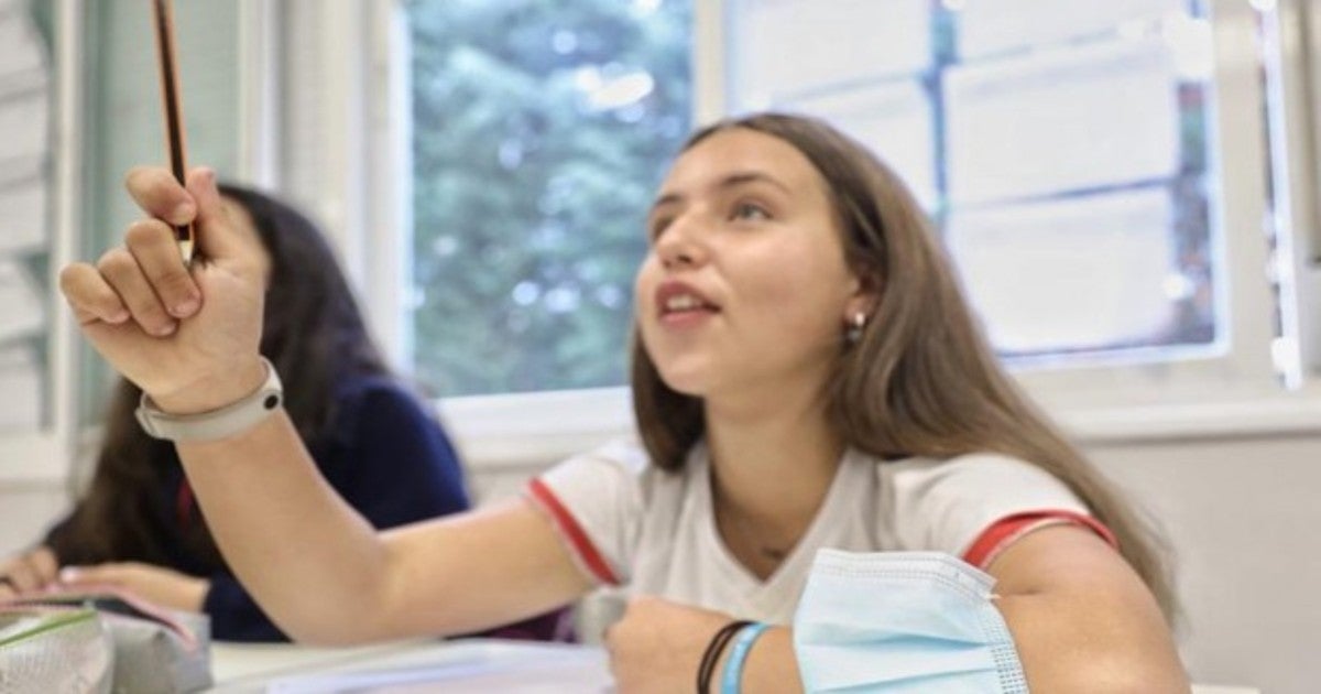 Una joven en un aula con la mascarilla en el brazo