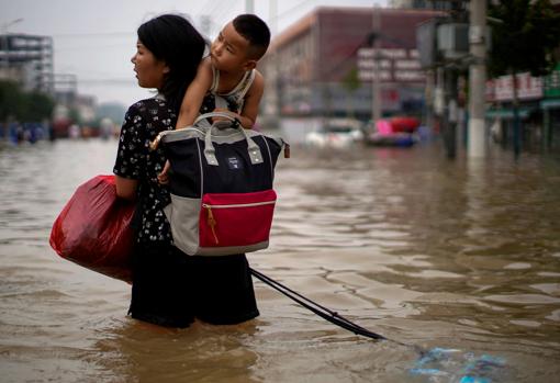 Una mujer carga con su hijo en unas inundaciones en China