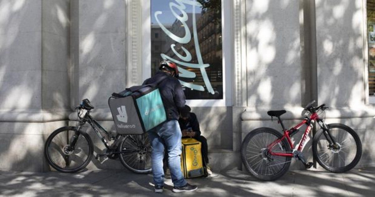 Dos repartidores de distintas empresas esperan a las puertas de un McDonald