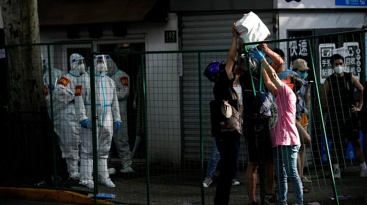 Un hombre traslada víveres a residentes de otra área por encima de las barreras de bloqueo, ayer en Shanghái