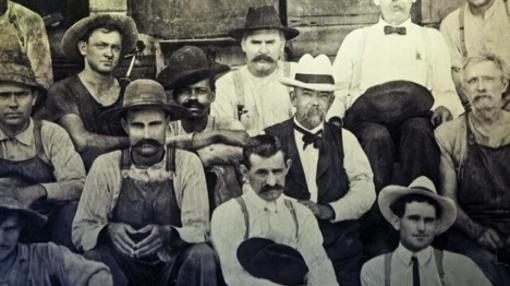 Fotografía tomada en 1900. Jack Daniel (hombre de barba y sombrero blanco del centro), sentado junto a un hombre afroamericano. Se cree que es George Green, hijo de Nearest Green