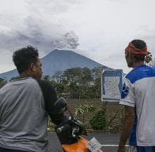 Dos vecinos observan el volcán Monte Agung arrojando ceniza volcánica caliente, visto desde Datah