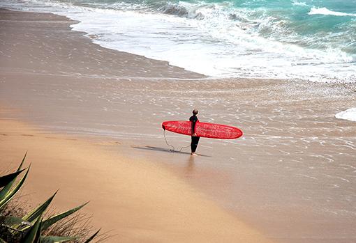 Un hombre lleva su tabla para surfear en la playa La Hierbabuena